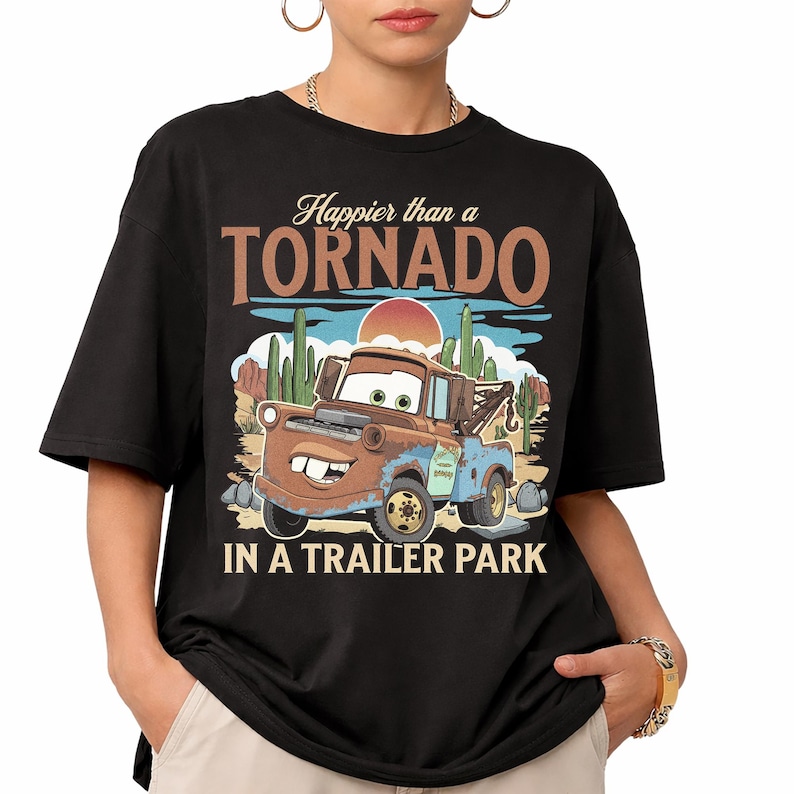 May include: Black t-shirt with a cartoon image of Mater from the film Cars, and the text "Happier than a Tornado in a Trailer Park." The design includes a desert landscape with cacti and a setting sun.