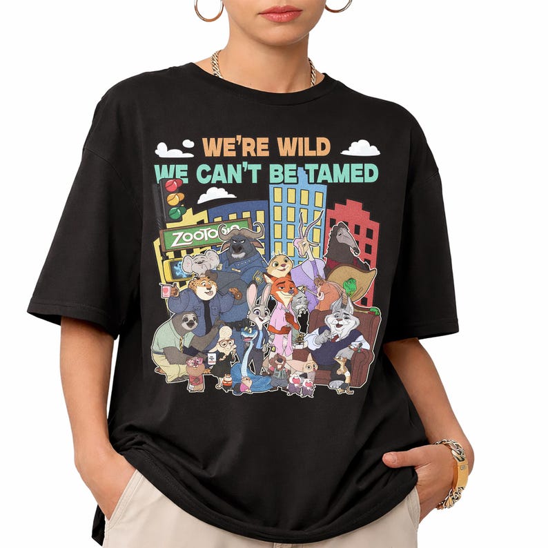 May include: Black t-shirt featuring a colorful graphic of characters from the animated film Zootopia. The design includes the text "WE'RE WILD WE CAN'T BE TAMED" above the cityscape and characters. The shirt is a casual wear item.