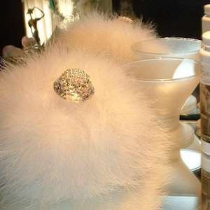 May include: A fluffy, white powder puff with a large, sparkling jewel. Two martini glasses and a bottle of "Ronditions" dusting powder are also visible. The items are arranged on a reflective surface.
