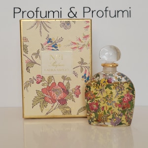 May include: A vintage perfume bottle and box set. The bottle is clear with a floral design, a gold neck, and a clear, round stopper. The box is beige with a floral pattern and the text "No. 1 Parfum Laura Ashley". The text "Profumi & Profumi" is at the top.