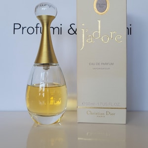 Peut inclure: Un ensemble de parfum avec flacon et boîte. Le flacon en verre transparent a un col doré et un dessus sphérique. La boîte est crème avec des lettres dorées qui disent "J'adore" et "Christian Dior". Le flacon contient 50 ml de parfum.
