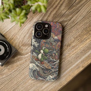 May include: A phone case featuring a colorful Japanese-inspired design with a green Yoshi character surfing on a wooden board. The case has a detailed illustration of waves, a dragon, and a mountain.