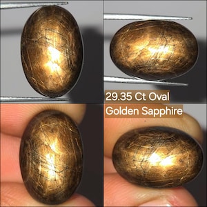 Può includere: Una gemma di zaffiro dorato ovale da 29,35 ct con una superficie liscia e lucida. La pietra presenta una tavolozza di colori marrone caldo e oro intenso con inclusioni interne visibili e motivi venati naturali su tutta la forma ovale.