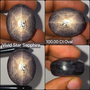 Op de afbeelding: Een 100,00 ct ovale Vivid Star Saffier edelsteen met een donkergrijs-paarse tint en een zichtbaar zespuntig stereffect. De steen heeft een glad, gepolijst cabochon oppervlak met natuurlijke insluitingen en een rond profiel.