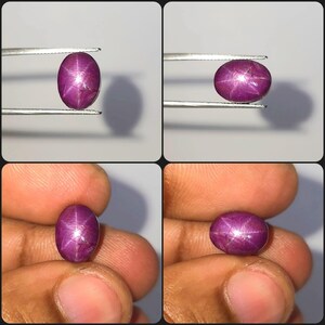 Pode incluir: Uma pedra preciosa de rubi estrela de formato oval e cor magenta profunda, apresentando um efeito de estrela de seis raios distinto em sua superfície cabochão. A gema é exibida de vários ângulos, segurada por pinças de metal.