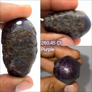 May include: A raw, deep purple gemstone with a rough, textured surface and polished sections. The stone is labeled as 260.45 Ct and purple. It displays a dark, opaque appearance with natural mineral inclusions and a visible star-like light reflection.