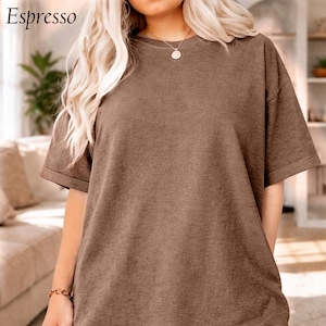 May include: A short-sleeved, espresso-coloured t-shirt. The shirt has a crew neck and a relaxed fit. The word "Espresso" is in the upper left corner. The model is wearing a gold necklace and bracelet.