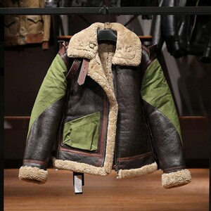 Puede incluir: Chaqueta de cuero marrón y verde con cuello y forro de borrego beige. La chaqueta tiene cremallera frontal, bolsillo y ribetes de cuero marrón. Las mangas son verdes con detalles de cuero marrón. La chaqueta está colgada.