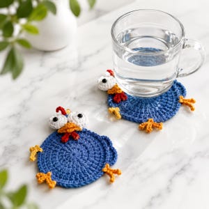 May include: Two round blue crochet coasters shaped like chickens, featuring white eyes with black pupils, orange beaks, red combs, and small orange feet extending from the sides. One coaster supports a clear glass mug filled with water.
