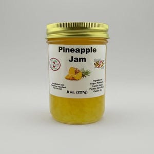 May include: A jar of pineapple jam with a gold lid. The label reads "Pineapple Jam" with an illustration of pineapple slices and a sprig of rosemary. The jar contains 8 oz. (227g) of jam.