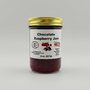 Könnte beinhalten: Ein Glas Schoko-Himbeer-Marmelade mit goldenem Deckel. Das Etikett trägt die Aufschrift "Chocolate Raspberry Jam" mit Bildern von Himbeeren und Schokolade. Das Glas enthält 227g Marmelade.