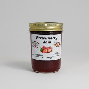 Könnte beinhalten: Ein Glas Erdbeermarmelade mit goldenem Deckel. Das Etikett trägt die Aufschrift "Strawberry Jam" und zeigt eine Abbildung von Erdbeeren. Das Glas enthält 227g Marmelade.