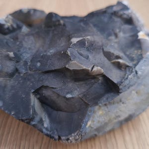 以下が含まれることがあります： 表面がざらざらとした、凹凸のある濃い灰色のフリントロック。石は、より明るい灰色と白のインクルージョンを持つ層状の外観をしています。この岩は、おそらく先史時代の道具または人工物です。