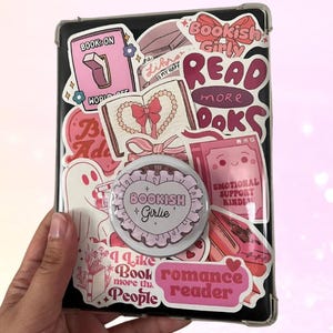 May include: A white ceramic mug with a black handle and the text "But First, Coffee" in a black, handwritten-style font. The mug is on a white surface.