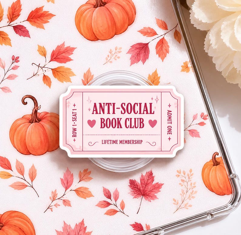 May include: A pink and white ticket-shaped phone grip with the text "ANTI-SOCIAL BOOK CLUB" and "LIFETIME MEMBERSHIP". The background features pumpkins and fall leaves in orange, red, and yellow.