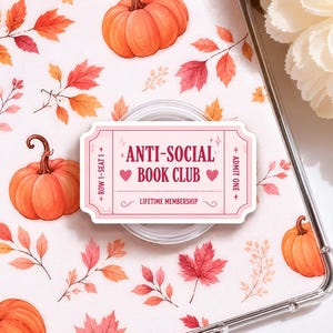 May include: A pink and white ticket-shaped phone grip with the text "ANTI-SOCIAL BOOK CLUB" and "LIFETIME MEMBERSHIP". The background features pumpkins and fall leaves in orange, red, and yellow.