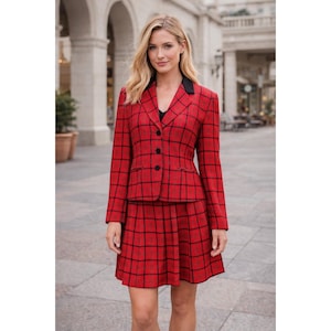 Op de afbeelding: Een rood geruit blazer en bijpassende rok. De blazer heeft een zwarte kraag en zwarte knopen. De rok is een geplooide minirok. De outfit is een klassieke, op maat gemaakte stijl.