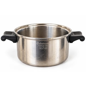 Può includere: Una pentola in acciaio inossidabile con due manici laterali neri. Sul lato della pentola è presente il testo inciso: Saladmaster, STAINLESS STEEL, 18-8 TRI-CLAD, DALLAS, TEXAS. La pentola ha una finitura metallica lucida e un'ampia apertura.