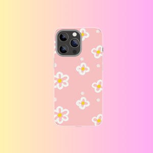 Peut inclure: Une coque de téléphone rose avec un motif floral. La coque présente des fleurs blanches avec des centres jaunes et de petits points blancs. La coque de téléphone a un module caméra avec trois lentilles.