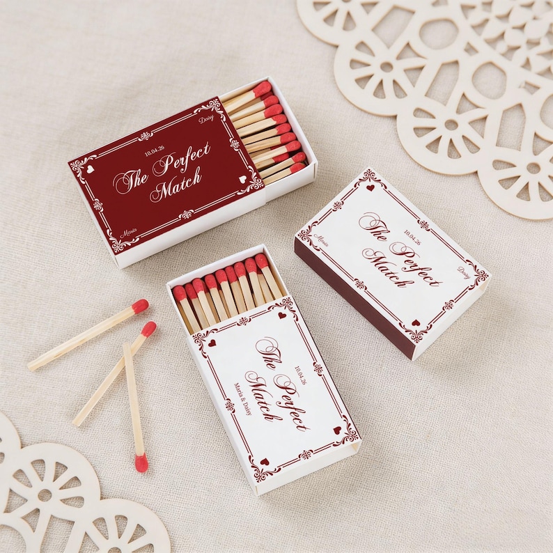 May include: Three white matchboxes with red and burgundy accents, each containing wooden matches with red tips. The boxes feature the text "The Perfect Match" in elegant script, with decorative borders and hearts. The date "10.04.26" is also visible.