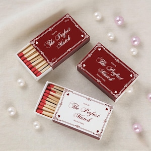 May include: Three red matchboxes with the text "The Perfect Match" and the date 10.04.26. The matchboxes are open, revealing red-tipped matches. Pearls are scattered around the matchboxes.