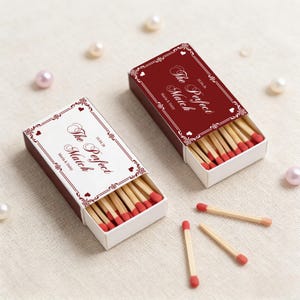 May include: Two open matchboxes with the text "The Perfect Match" and the date 10.04.20, along with the names Maria & Daisy. The matchboxes are burgundy with white and burgundy decorative borders. Several matches are scattered around.