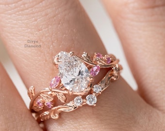 Könnte beinhalten: Verlobungsring-Set aus Roségold mit einem birnenförmigen Diamanten und rosa Edelsteinakzenten. Der Ring hat ein florales Design mit dem Text "Divya Diamond".