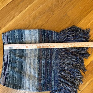 May include: A knitted scarf with a striped pattern in shades of blue, grey, and brown. The scarf has a fringed edge. The Home Depot ruler shows the scarf is approximately 30 cm long.