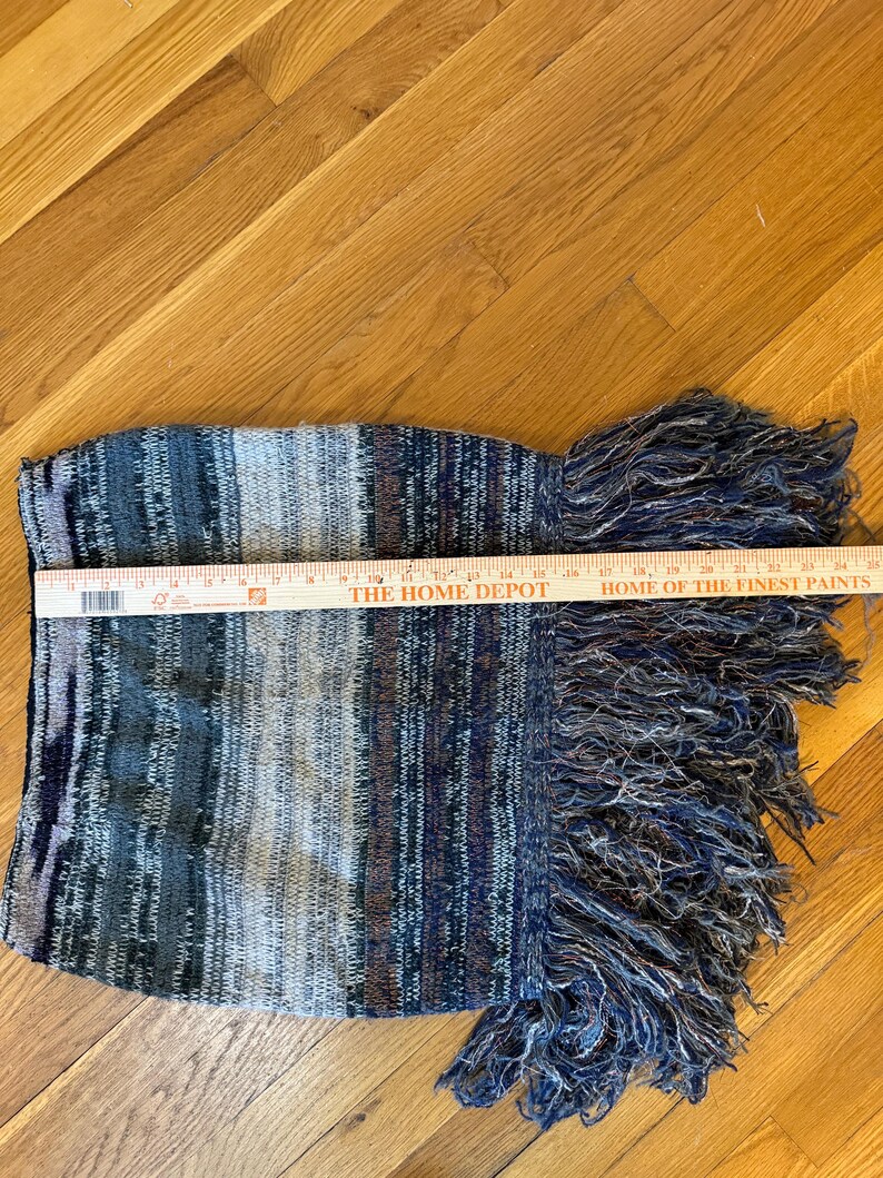 May include: A knitted scarf with a striped pattern in shades of blue, grey, and brown. The scarf has a fringed edge. The Home Depot ruler shows the scarf is approximately 30 cm long.