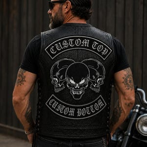May include: A black leather vest featuring a textured finish and side lacing. The back displays a large embroidered graphic of three skulls with white outlines. Two arched patches are sewn above and below the skulls, reading CUSTOM TOP and CUSTOM BOTTOM in a bold, gothic-style white font.
