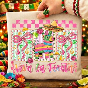 Puede incluir: Un cojín beige con un diseño de fiesta colorido. El diseño incluye una piñata, un sombrero, un cóctel y el texto "Viva la Fiesta" en rosa. Lazos rosas y rosas decoran los bordes.