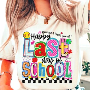 Pode incluir: Camiseta branca com um gr&aacute;fico colorido que diz "Happy Last Day of School". O design inclui um smiley, um l&aacute;pis, uma ma&ccedil;&atilde; e outros elementos escolares. O texto "Have fun! I love you all!" tamb&eacute;m est&aacute; inclu&iacute;do.