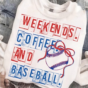 May include: White sweatshirt with the words "Weekends! Coffee and Baseball!" in red and blue block letters. A baseball with red and blue accents is also featured on the shirt. The sweatshirt is displayed on a denim jacket.