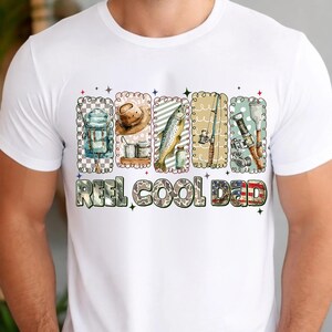 May include: White t-shirt featuring a colorful graphic of fishing-related items. The design includes a backpack, hat, fish, fishing rod, and other gear. The text "REEL COOL DAD" is printed below the images in a camouflage font.