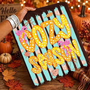 May include: A rectangular sign featuring the text "COZY SEASON" in large, yellow, white-polka-dotted letters. The background consists of vertical black and light blue stripes, decorated with pink bows, small orange pumpkins, and autumn leaves.