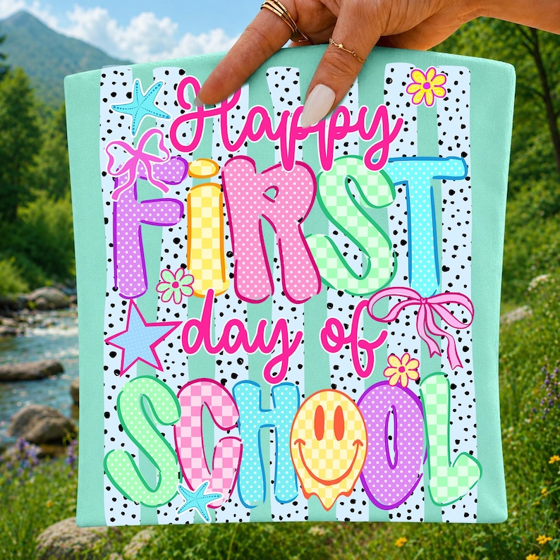 May include: A rectangular mint green fabric sign featuring the text Happy First day of SCHOOL in colorful, patterned bubble letters. The design includes black polka dots, vertical stripes, pink bows, yellow flowers, blue starfish, and a smiley face.