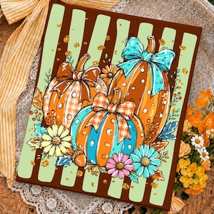 May include: A rectangular print featuring three pumpkins decorated with bows, set against a background of vertical brown and light green stripes. The pumpkins are orange and teal with white polka dots, accented by yellow, pink, and teal flowers.