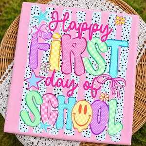 May include: A rectangular fabric panel featuring a pink background with vertical black polka-dot stripes. The text reads Happy FIRST day of SCHOOL in colorful, patterned letters. Decorative elements include a starfish, bow, and smiley face.