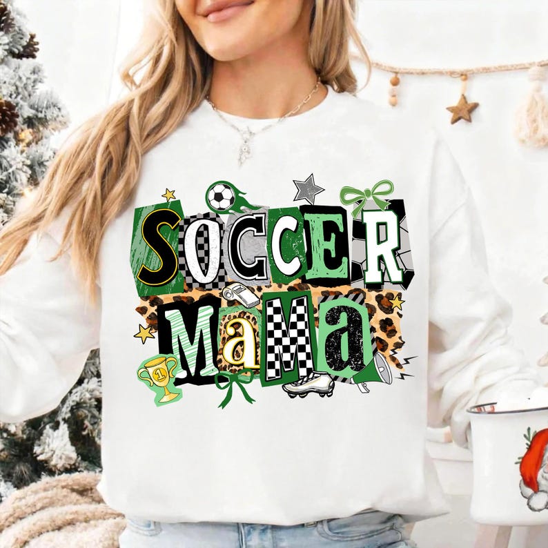 May include: White sweatshirt featuring the text "SOCCER Mama" in a green, black, and white design. The design incorporates soccer balls, stars, a trophy, and a leopard print pattern. The sweatshirt is a casual, sporty style.