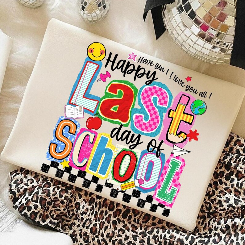 Pode incluir: Um moletom creme com um gr&aacute;fico colorido que diz "Happy Last Day of School". O design inclui um rosto sorridente, uma ma&ccedil;&atilde;, um l&aacute;pis e outros elementos com tema escolar. O texto "Have fun! I love you all!" tamb&eacute;m est&aacute; inclu&iacute;do.