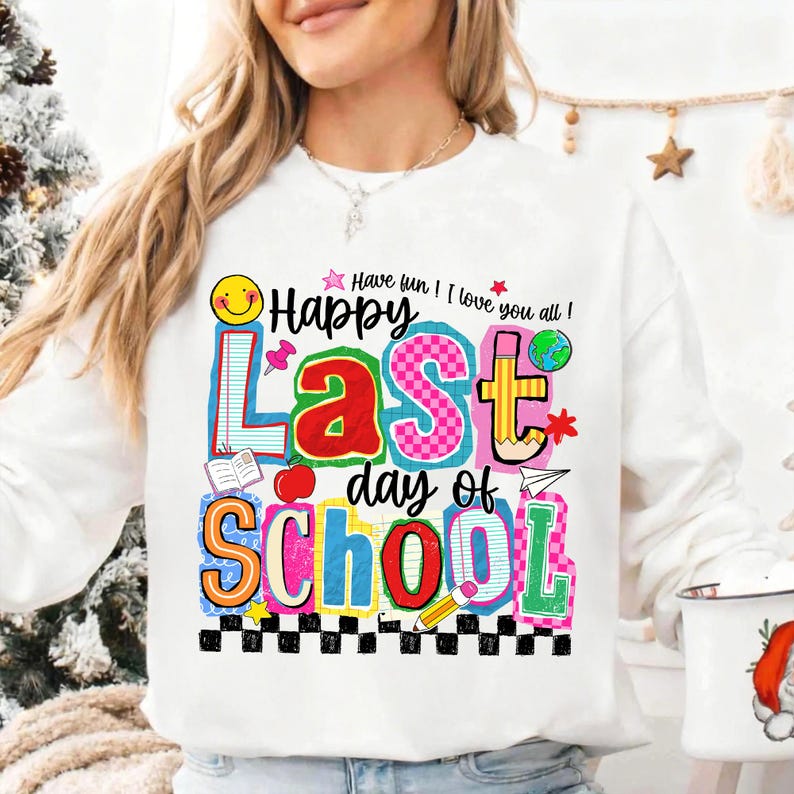 Pode incluir: Camisola branca com um gr&aacute;fico colorido que diz "Happy Last Day of School". O design inclui um rosto sorridente, um l&aacute;pis, uma ma&ccedil;&atilde; e as palavras "Have fun! I love you all!" em uma fonte divertida. A parte inferior do design tem um padr&atilde;o xadrez em preto e branco.