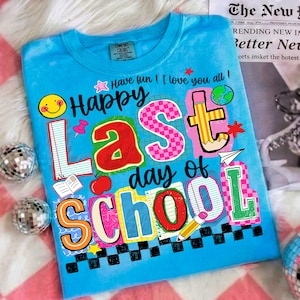 Pode incluir: Uma camiseta azul clara com um gr&aacute;fico colorido que diz "Happy Last day of School". O design inclui um smiley, um l&aacute;pis, uma ma&ccedil;&atilde; e outros elementos escolares. A camisa tamb&eacute;m tem o texto "Have fun! I love you all!"