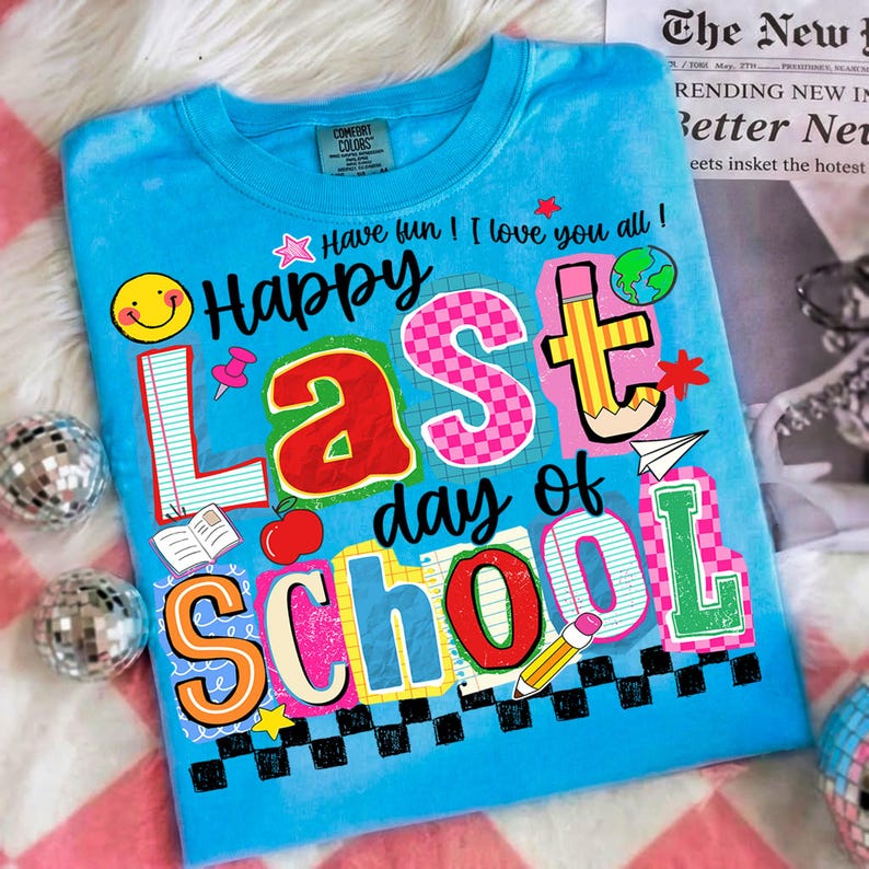 Pode incluir: Uma camiseta azul clara com um gr&aacute;fico colorido que diz "Happy Last day of School". O design inclui um smiley, um l&aacute;pis, uma ma&ccedil;&atilde; e outros elementos escolares. A camisa tamb&eacute;m tem o texto "Have fun! I love you all!"