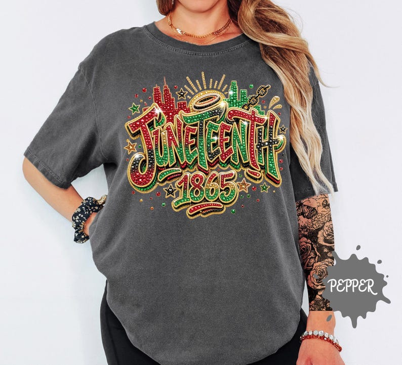 A person wearing a grey t-shirt with a colorful graphic design that says "JUNEEENTH 1865" and includes various decorative elements such as stars, flowers, and a city skyline.