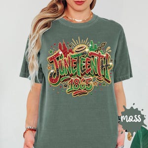 A woman wearing a green t-shirt with a colorful graphic design that says "JUNEENTH 1865" and includes various decorative elements such as stars, rays, and splashes of color.
