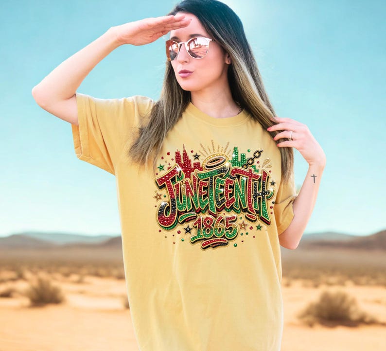 A woman wearing a yellow t-shirt with a graphic design and text, standing in a desert landscape with mountains in the background.