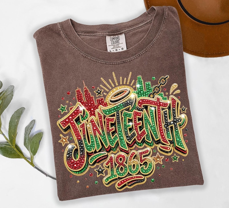 A brown t-shirt with a colorful graphic design featuring the text "JUNEENTH 1865" and decorative elements such as stars and lightning bolts.