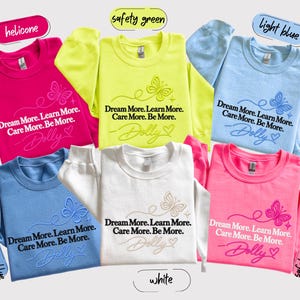 A collage of six colorful t-shirts with the same design, featuring the text "Dream More. Learn More. Care More. Be More." printed on them.