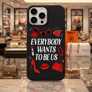 May include: Black phone case with the text "EVERYBODY WANTS TO BE US" in white. Red lipstick, high heels, sunglasses, and a handbag are illustrated on the case. The case has a glossy finish and is designed for a smartphone.