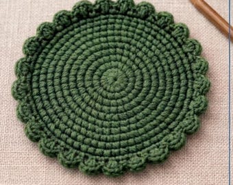 Könnte beinhalten: Ein handgefertigter, grüner Häkeluntersetzer mit strukturiertem Rand. Der Untersetzer ist rund mit einem Spiralmuster in der Mitte. Der Text "CROCHET COASTER PATTERN" steht oben, darunter "Beginner Friendly Round Coaster with Textured Edge".